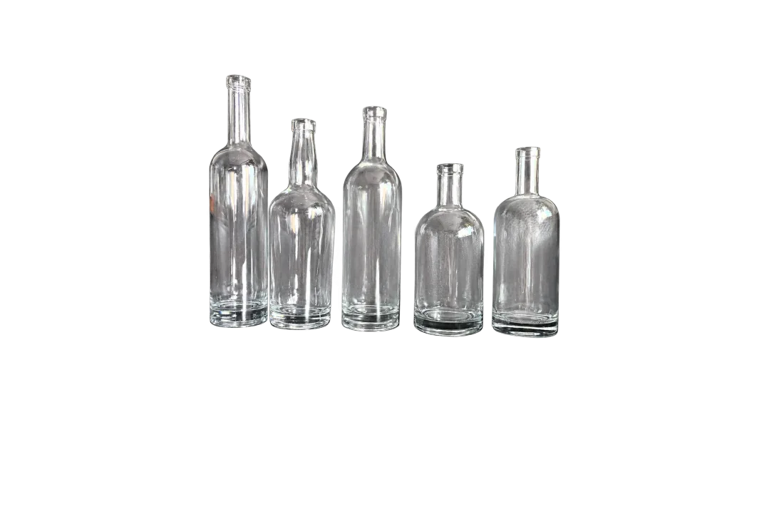 Five empty clear glass bottles with varied rounded body shapes arranged side by side on a dark surface