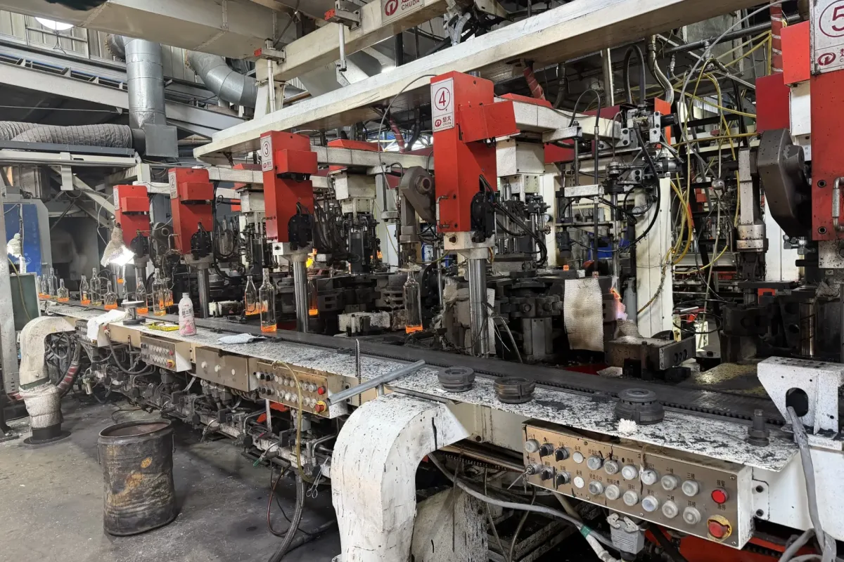 CHUDA glass bottle production line with clear bottles on a conveyor and numbered red forming stations.