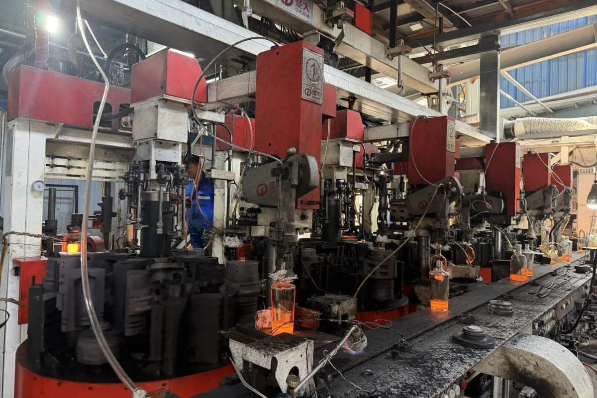CHUDA glass container forming machines with hot glass containers moving along an industrial production line.