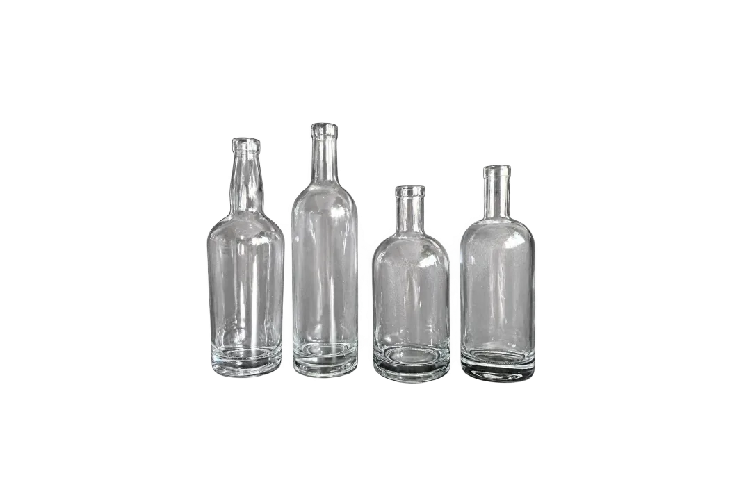 Four empty clear glass bottles with varied body shapes arranged against a dark background