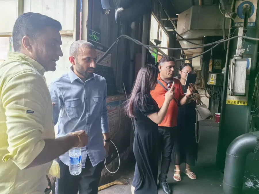 Five people inspect large green industrial machinery inside a factory.