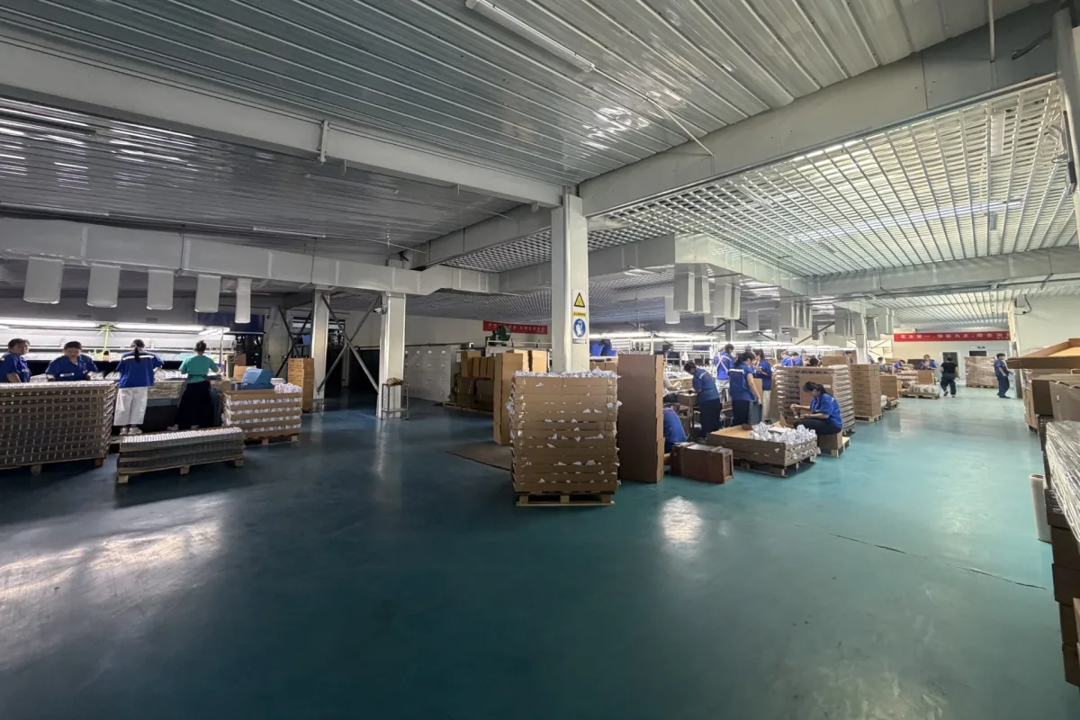 Factory production and packing area with workers, workstations, cardboard cartons, and palletized loads