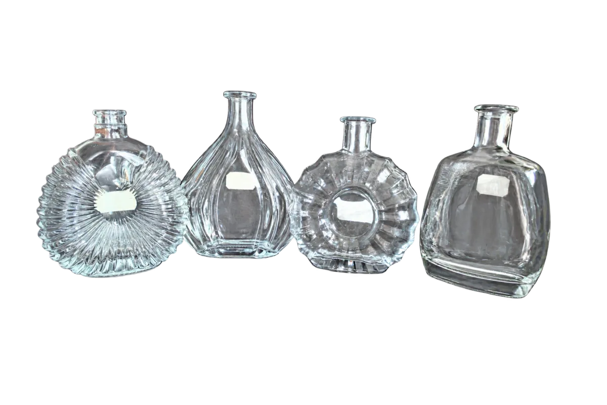 Four clear decorative glass bottles with faceted and fluted designs arranged on a dark leather seat