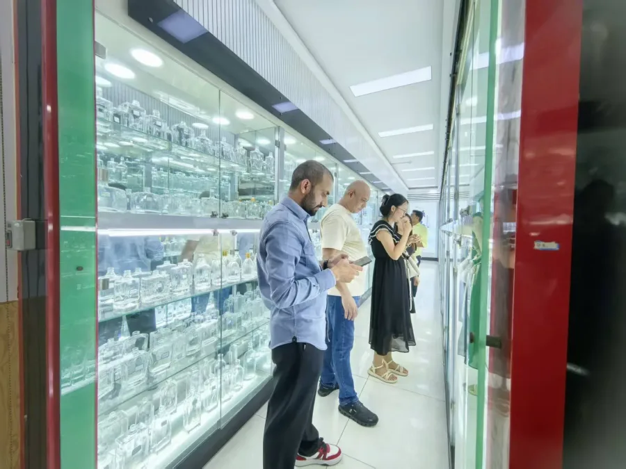 Illuminated showroom cabinets displaying assorted transparent glass containers while visitors examine them
