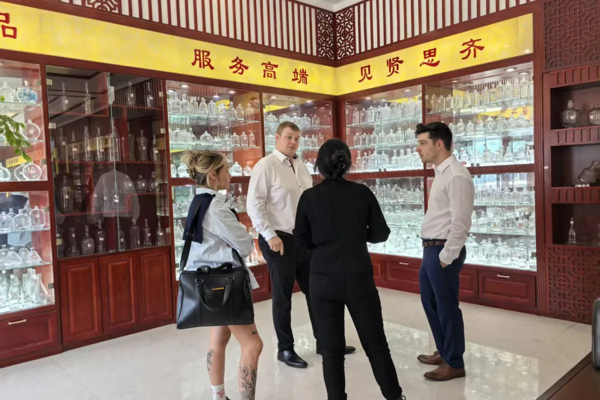 Glass bottles and containers arranged in illuminated wooden showroom cabinets with four people standing in front.