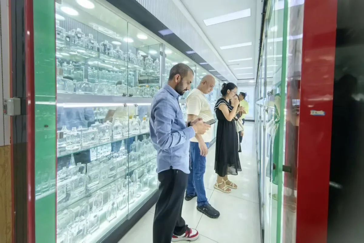 Illuminated showroom cabinets displaying assorted transparent glass containers while visitors examine them